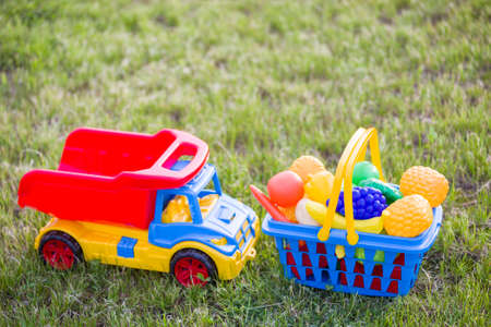 Car truckand a basket with toy fruit and vegetables. Bright plastic colorful toys for children outdoors on sunny summer day.の写真素材