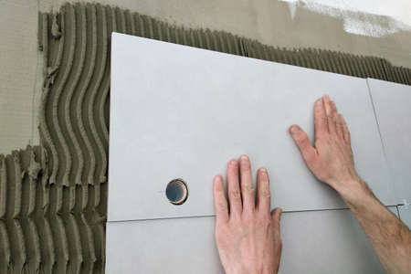 Worker hands putting ceramic tiles on the wall.