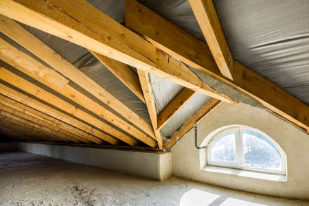 Attic of a building with wooden beams of a roof structure and a small window.