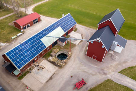 Top view of rural landscape on sunny spring day. Farm with solar photo voltaic panels system on wooden building, barn or house roof. Green field copy space background. Renewable energy production.の写真素材