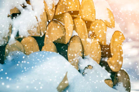 Neatly piled stack of chopped dry trunks wood covered with snow outdoors on bright cold winter sunny day, big snowflakes abstract background, Fire wood logs prepared for winter, ready for burning.の写真素材