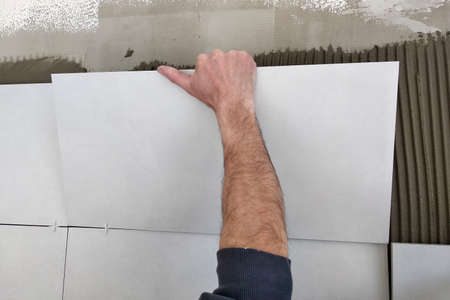Worker hands putting ceramic tiles on the wall.
