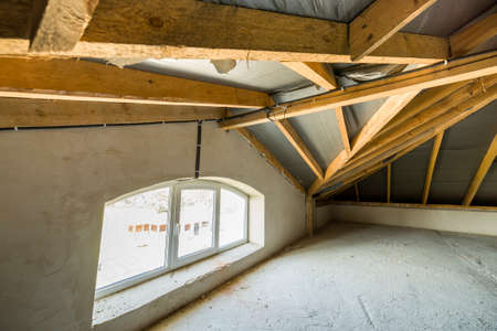 Attic of a building with wooden beams of a roof structure and a small window.
