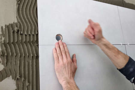 Worker hands putting ceramic tiles on the wall.
