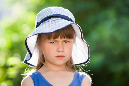 Close-up portrait of serious little girl in a big hat. Child having fun time outdoors in summer.の写真素材
