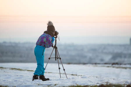 Child boy taking pictures outside in winter with photo camera on a tripod on snow covered field.の写真素材
