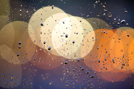 Abstract colorful bokeh background with yellow circles and water drops on glass surface in front....