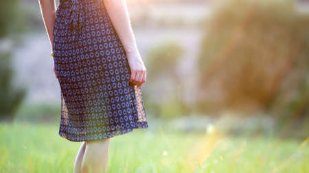 Young woman standing alone on a field with green grass enjoying warm sunset.の写真素材