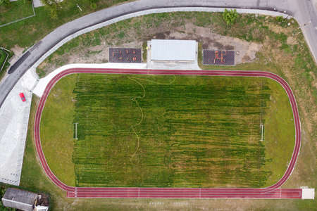 Aerial view of a football field on a stadium covered with green grass in rural town area.