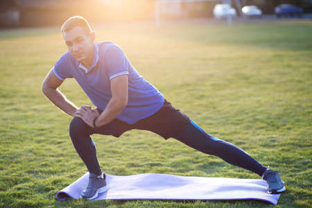 Young sportive man doing stretching exercises before running in morning field outdoors.