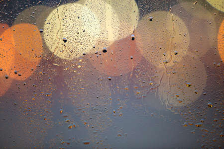 Abstract colorful bokeh background with yellow circles and water drops on glass surface in front. Blurred city lights.