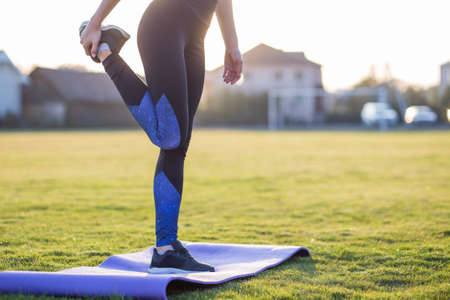 Closeup of young sportive woman doing exercise before running in morning field outdoors.