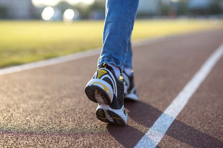 Close up of woman feet in sport sneakers and blue jeans on running lane on outdoor sports court.