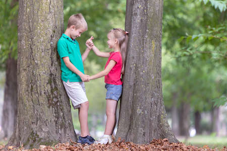 Portrait of two pretty cute children boy and girl standing near big tree trunk in summer park outdoors.の写真素材