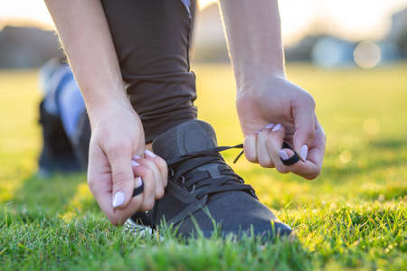Close-up of female hands tying shoelace on running shoes before practice. Runner getting ready for...
