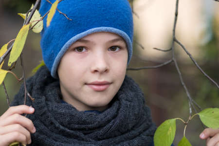 Pretty child boy wearing warm winter clothes holding tree branch with green leaves in cold weather outdoors.の写真素材