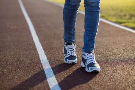 Close up of woman feet in sport sneakers and blue jeans on running lane on outdoor sports court.の写真素材