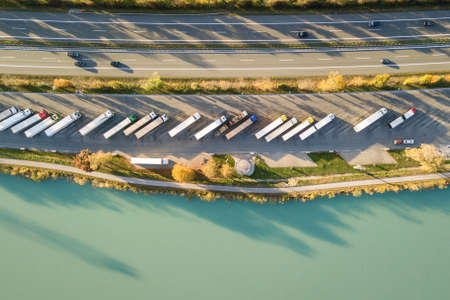 Top down aerial view of highway interstate road with fast moving traffic and parking lot with parked...