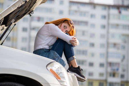 Young stressed woman driver near broken car with popped hood waiting for assistance.の写真素材
