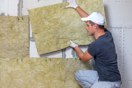 Worker insulating a room wall with mineral rock wool thermal insulation.の写真素材