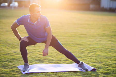 Young sportive man doing stretching exercises before running in morning field outdoors.