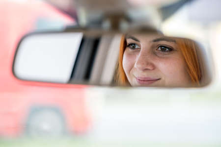 Young woman driver checking rear view mirror looking backwards while driving a car.