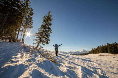 Hiker with raised arms standing in winter snow covered nature landscape enjoying view of distant...