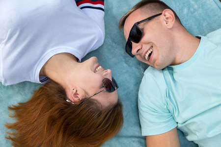 Young teenage couple in sunglasses laying together on blue cloth enjoying love relations.