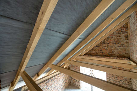 Attic space of a building under construction with wooden beams of a roof structure and brick walls....