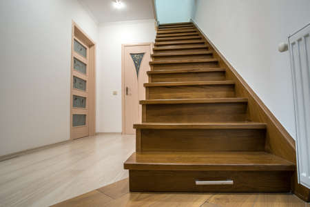 Modern architecture interior with luxury hallway with glossy wooden stairs in multi-storey house. Custom built pullout cabinets on glides in slots under stairs. Use of space for storage.のeditorial素材