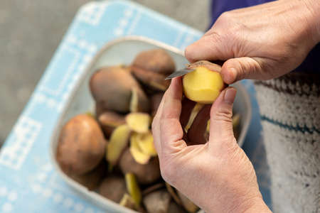 Closeup of woman hands peeling potatoes with a kitchen knife.の写真素材