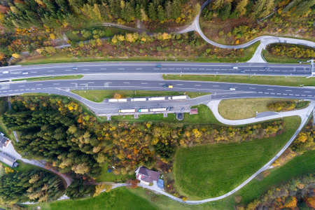 Top dawn aerial view of freeway speed road between yellow autumn forest trees in rural area.
