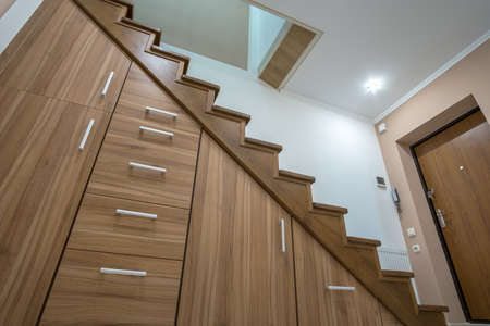 Modern architecture interior with luxury hallway with glossy wooden stairs in multi-storey house. Custom built pullout cabinets on glides in slots under stairs. Use of space for storage.の写真素材
