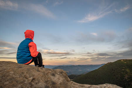 Young child boy hiker sitting in mountains enjoying view of amazing mountain landscape.の写真素材