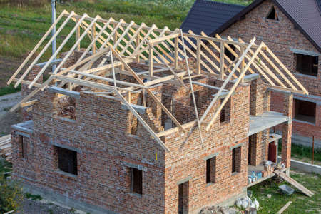Unfinished brick house with wooden roof structure under construction.の写真素材