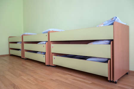 Many small beds with fresh linen in daycare preschool empty bedroom interior for comfortable...