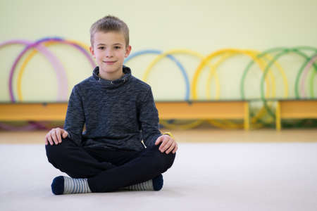 Young child boy sitting and relaxiong on the floor inside sports room in a school after training.の写真素材