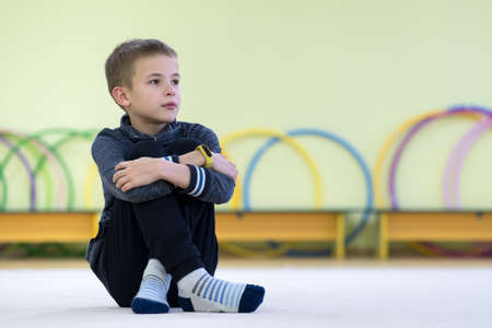 Young child boy sitting and relaxiong on the floor inside sports room in a school after training.の写真素材