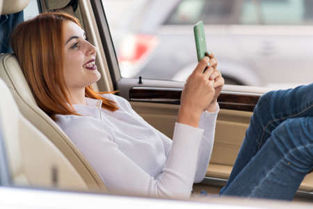 Young redhead woman driver taking selfies with her mobile phone sitting behind the wheel of the car...