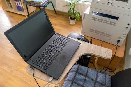 Open black laptop computer on a small chair table in office interior.