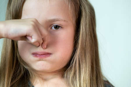 Close-up portrait of little girl with long hair holding her nose with fingers in disgust.の写真素材