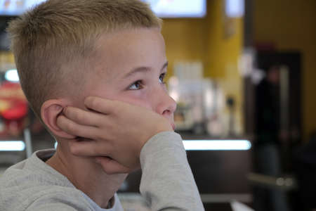 Child boy sitting in fast food restaurant behind empty table waiting for food.の写真素材