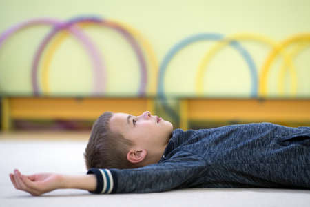 Young child boy laying down and relaxiong while resting on the floor inside sports room in a school...