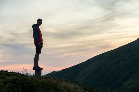 Dark silhouette of a hiker on a mountain at sunset standing on summit like a winner.