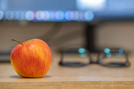 A red apple on office desk on computer screen blurred background.
