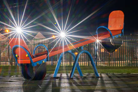 Seesaw swing in preschool yard with soft rubber flooring at night.の写真素材
