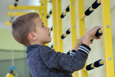 Young child boy exercising on a wall ladder bar inside sports gym room in a school.