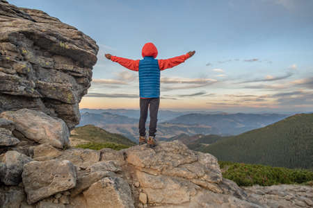 Young child boy hiker standing with raised hands in mountains enjoying view of amazing mountain landscape at sunset.の写真素材