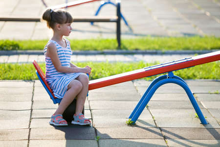 Cute young child girl outdoors on see-saw swing on sunny summer day.の写真素材