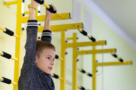 Young child boy exercising on a wall ladder bar inside sports gym room in a school.